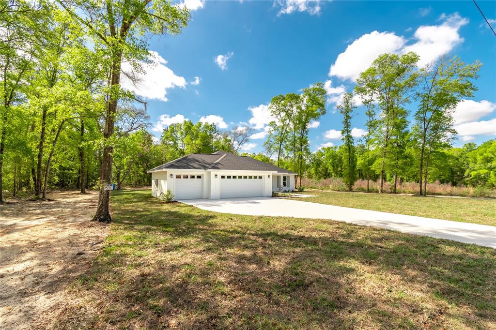 A white house with a three-car garage sits on a grassy lot surrounded by trees — 12440 SW 52ND LANE ROAD, OCALA, FL