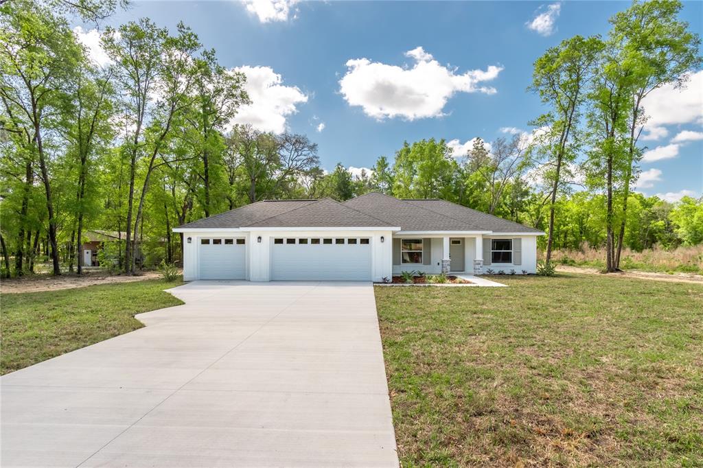 A white single-story house with a three-car garage sits on a grassy lot with trees — 12440 SW 52ND LANE ROAD, OCALA, FL