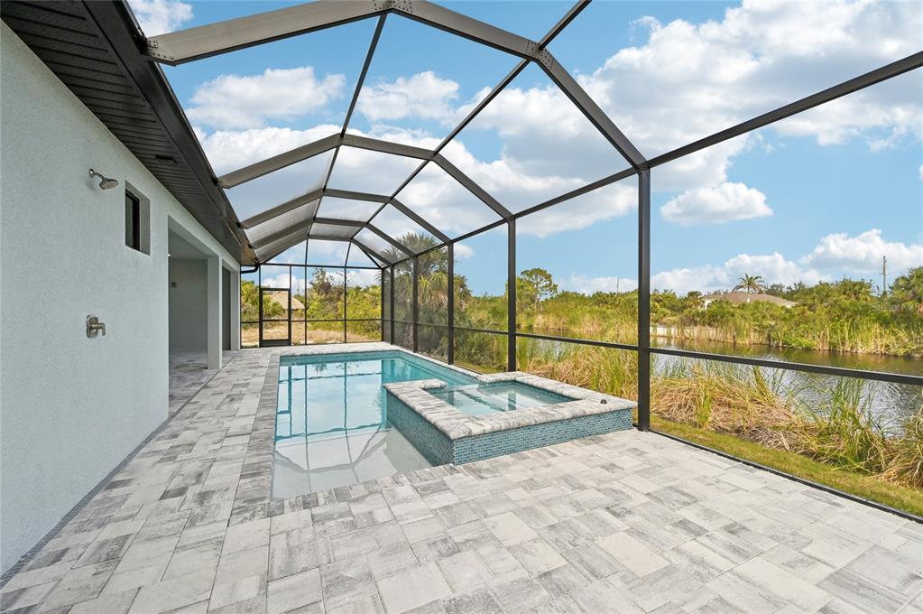 A screened-in pool and spa area with paver decking overlooking a pond — 9516 PRESIDENT CIRCLE, PORT CHARLOTTE, FL