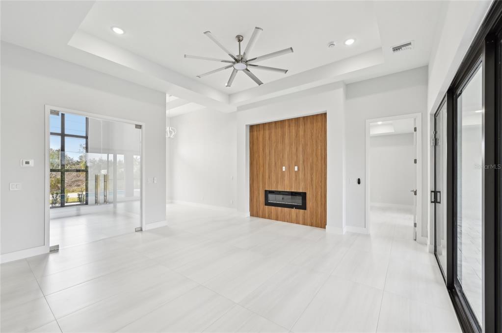 A modern living room features white tile floors, a tray ceiling, and a wood-paneled fireplace wall — 9516 PRESIDENT CIRCLE, PORT CHARLOTTE, FL