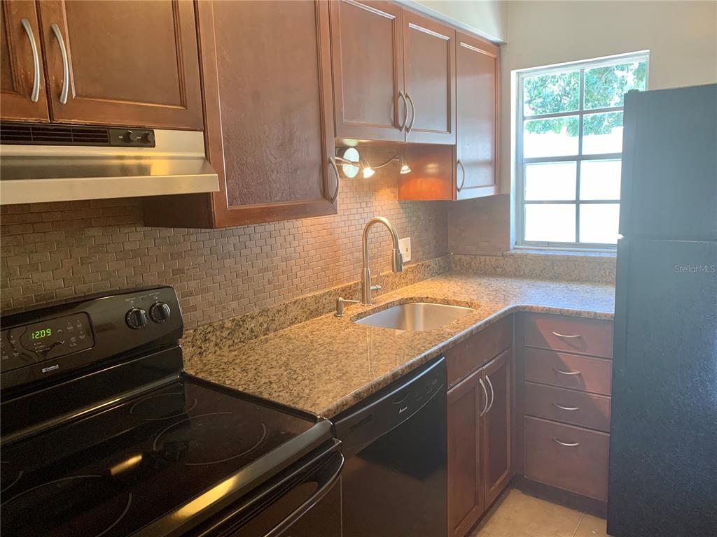 A kitchen features dark wood cabinets, granite countertops, a tiled backsplash, and black appliances — 525 CONWAY ROAD UNIT 9, ORLANDO, FL