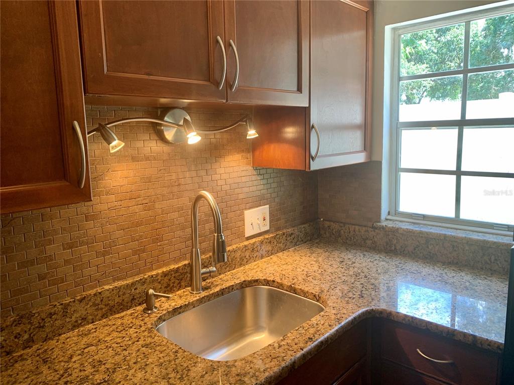 A kitchen sink with granite countertops and a tiled backsplash sits below wooden cabinets — 525 CONWAY ROAD UNIT 9, ORLANDO, FL