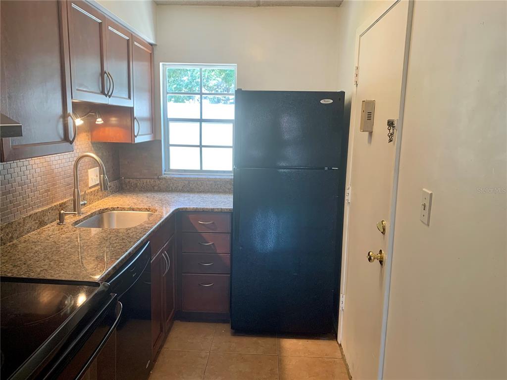 A kitchen features dark wood cabinets, granite countertops, a black refrigerator, and a tiled backsplash — 525 CONWAY ROAD UNIT 9, ORLANDO, FL