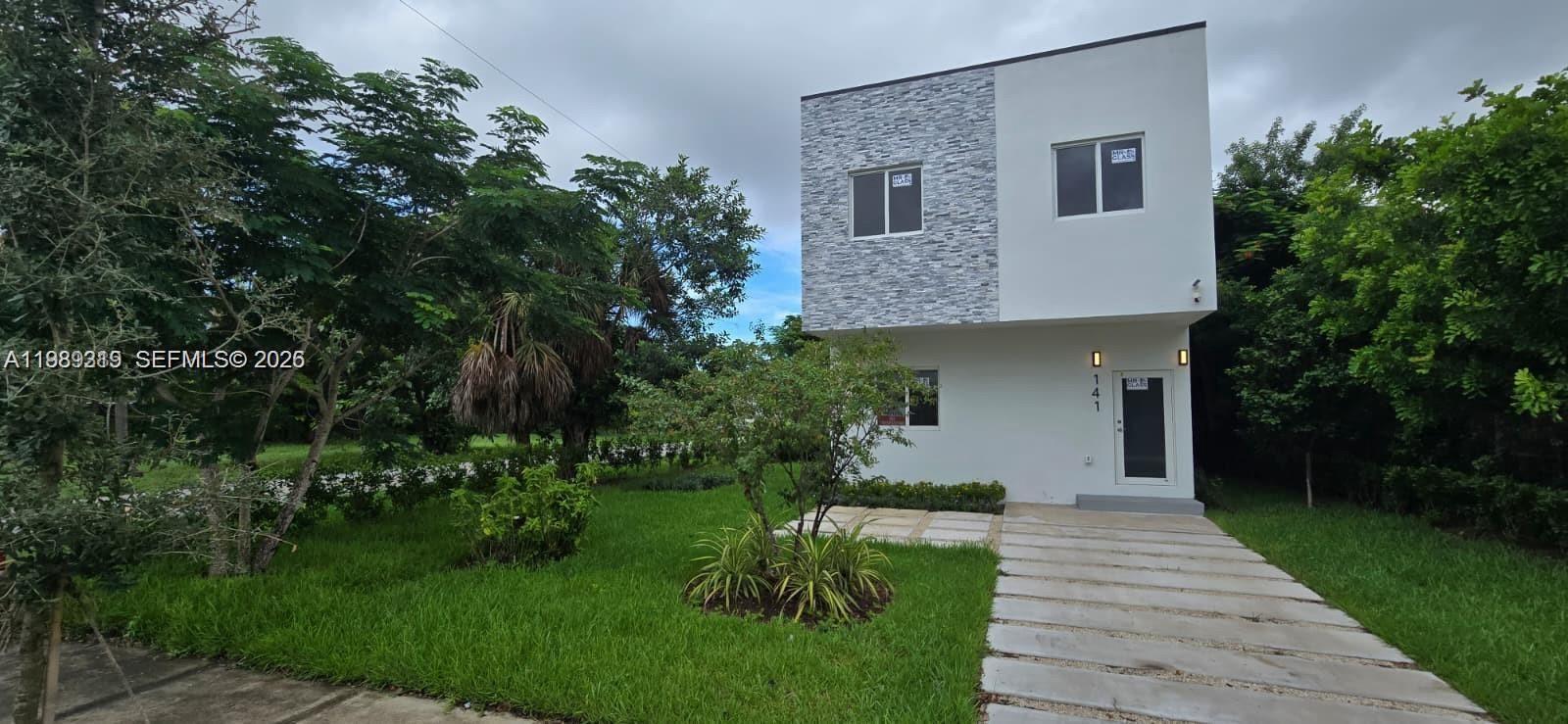 A two-story house with a stone-accented facade and a concrete walkway sits on a lawn — 141 NW 11th St, Pompano Beach FL 33060, POMPANO BEACH, FL