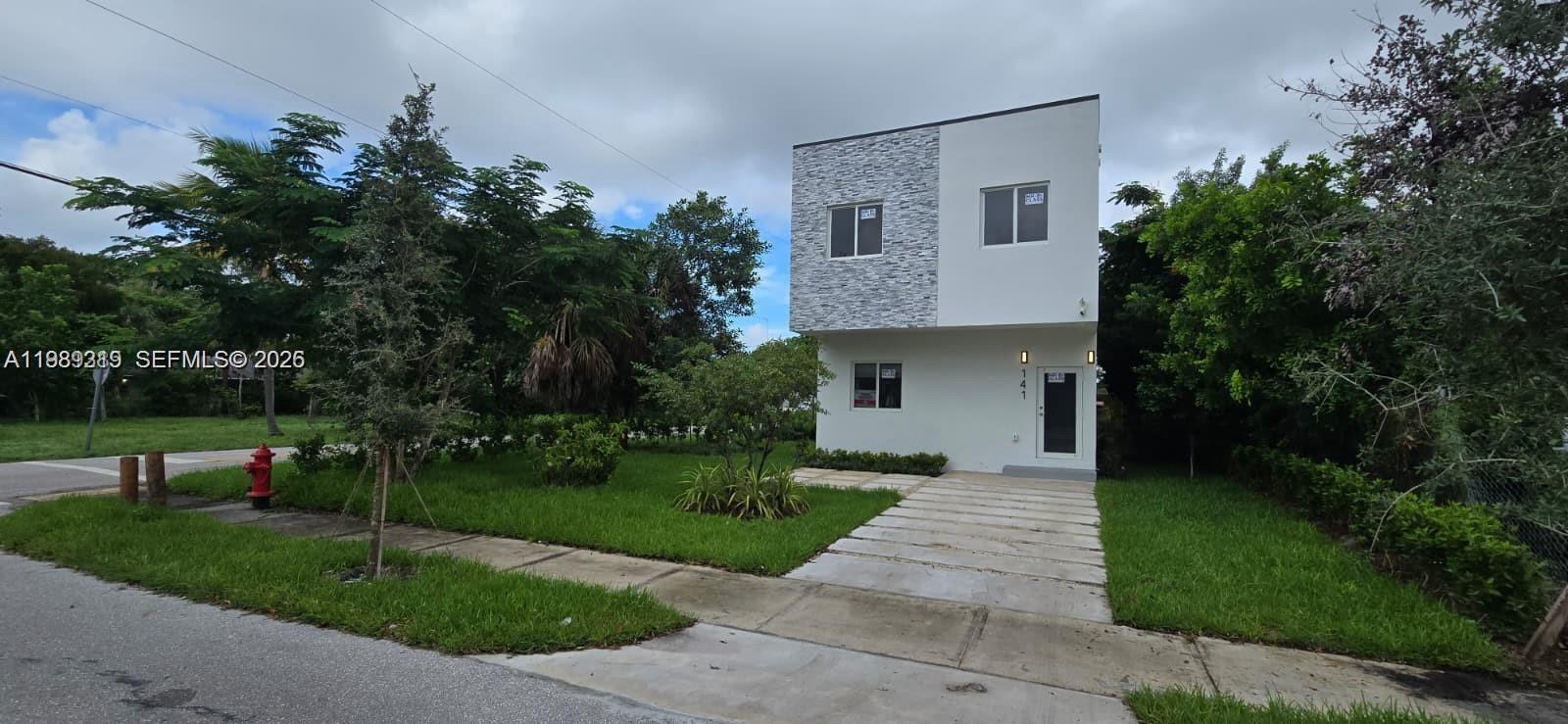 A two-story modern house with a stone-accented facade stands next to a concrete driveway — 141 NW 11th St, Pompano Beach FL 33060, POMPANO BEACH, FL