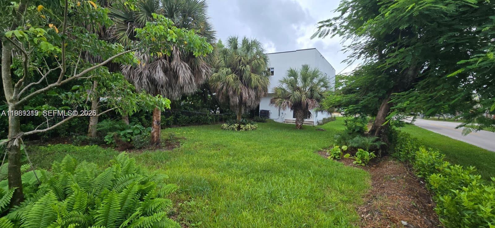 A white multi-story building stands behind a grassy yard with several palm trees — 141 NW 11th St, Pompano Beach FL 33060, POMPANO BEACH, FL