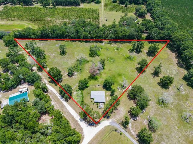 An aerial view shows a house situated on a large, triangular, tree-dotted grassy lot — 289 SW PURITAN PLACE, LAKE CITY, FL