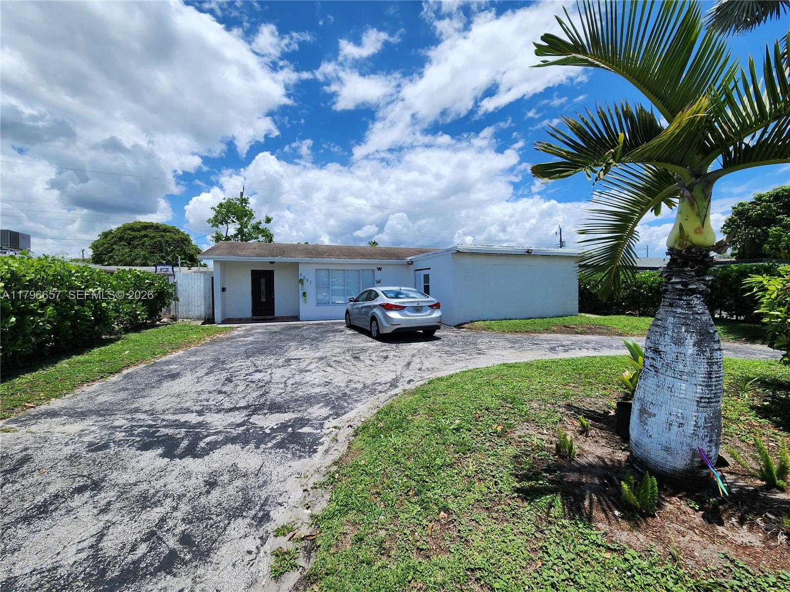 A single-story white house with a paved driveway and a palm tree in the foreground — 6881 Sheridan St, Hollywood FL 33024, HOLLYWOOD, FL