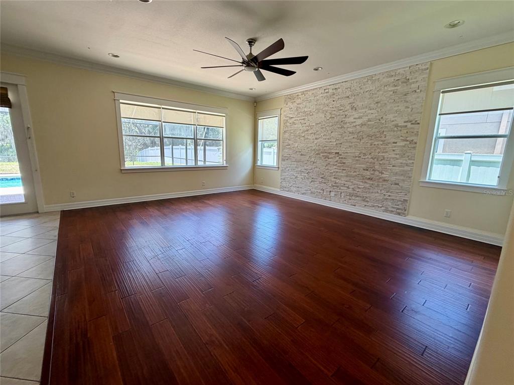 A living room features dark wood flooring, a stone accent wall, and a ceiling fan — 10531 MISTFLOWER LANE, TAMPA, FL