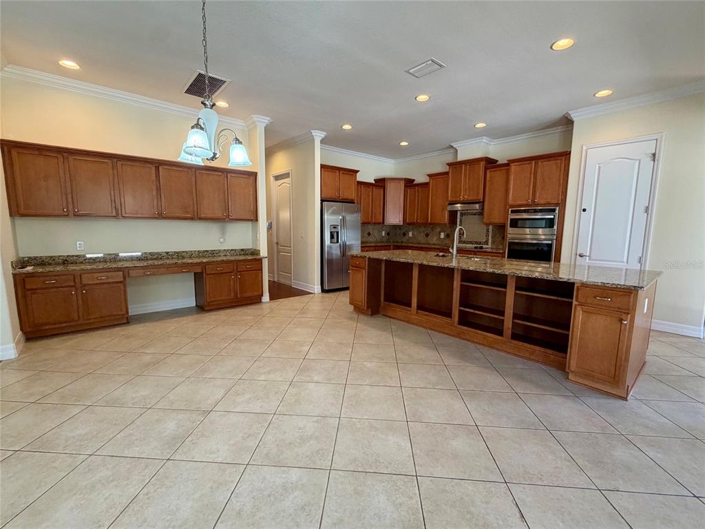 A kitchen features wood cabinetry, granite countertops, an island with open shelving, and tile flooring — 10531 MISTFLOWER LANE, TAMPA, FL