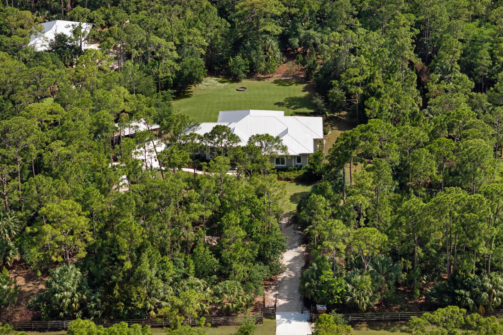 An aerial view of a house with a white metal roof surrounded by dense forest — 9010 Valley Oak Place, Jupiter FL 33478, JUPITER, FL