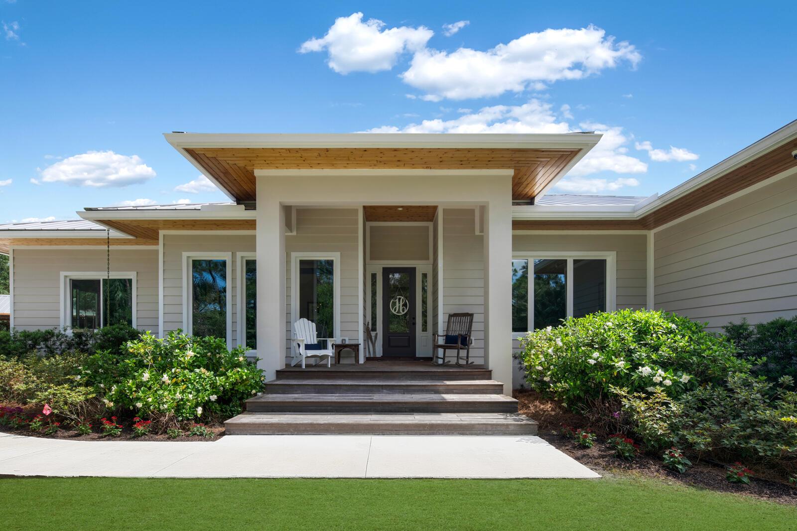 A modern house exterior features a wooden porch, white columns, and a landscaped front yard — 9010 Valley Oak Place, Jupiter FL 33478, JUPITER, FL