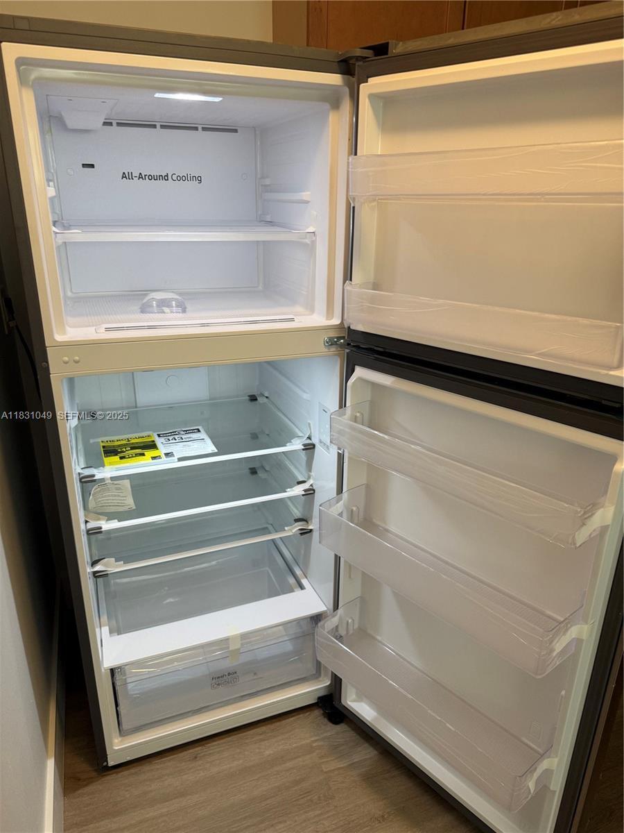An open, empty top-freezer refrigerator with glass shelves and interior lighting stands in a room — 67 Monaco B, Delray Beach FL 33446, DELRAY BEACH, FL