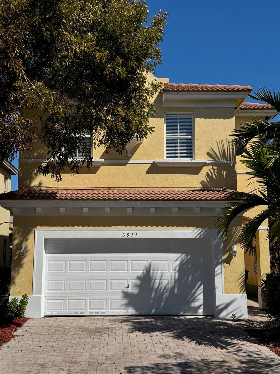 A two-story yellow stucco house with a white garage door and a paver driveway — 3977 NE 11th Drive, Homestead FL 33033, HOMESTEAD, FL