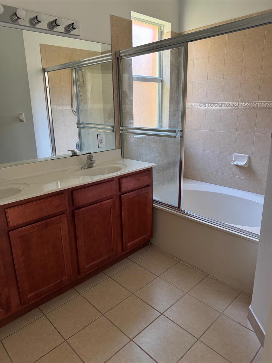 A bathroom features a double vanity with wood cabinets, a large mirror, and a shower-tub combo — 3977 NE 11th Drive, Homestead FL 33033, HOMESTEAD, FL