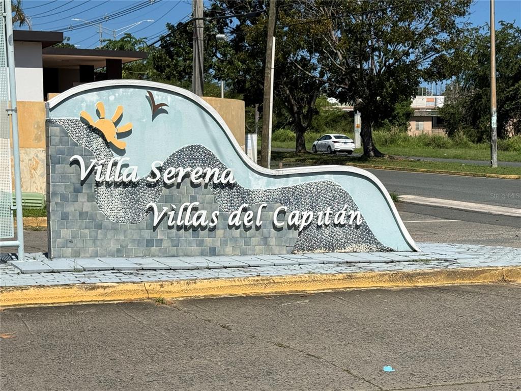 A curved monument sign for Villa Serena Villas del Capitán stands near a paved road — SR 659 Villas del Capitan SOLANDRA ST UNIT AA-12, ARECIBO, PR