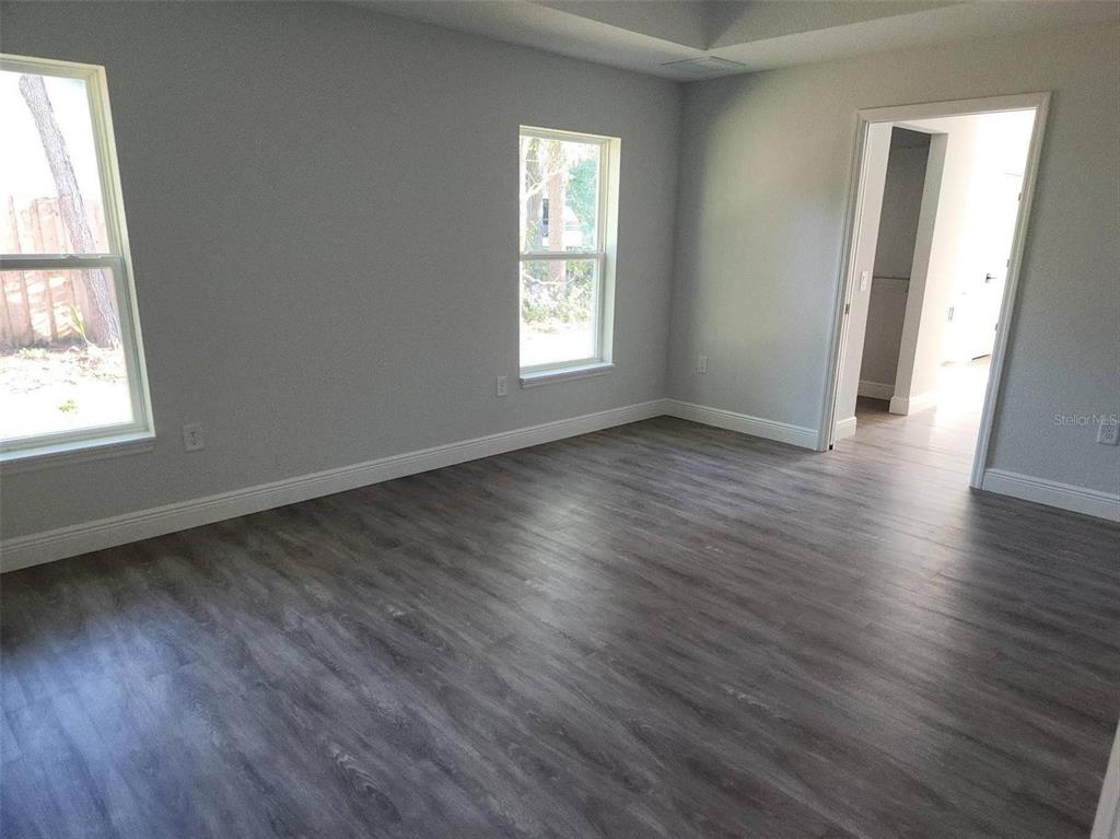 An empty bedroom features gray walls, wood-look flooring, two windows, and a doorway — 1111 DAGMAR AVENUE, SPRING HILL, FL