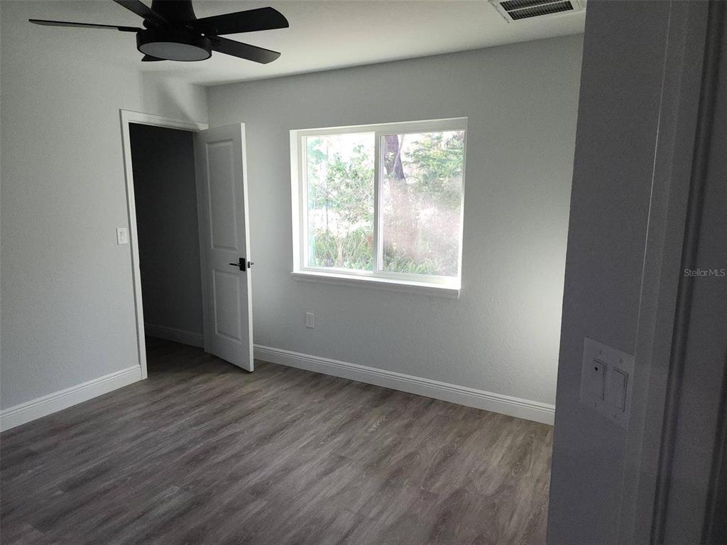 A bedroom with light gray walls, wood-look flooring, a ceiling fan, and a window — 1111 DAGMAR AVENUE, SPRING HILL, FL