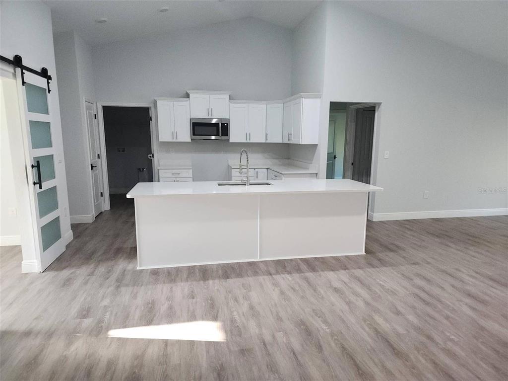 A modern kitchen features white cabinets, a central island, and light wood-look flooring — 1111 DAGMAR AVENUE, SPRING HILL, FL