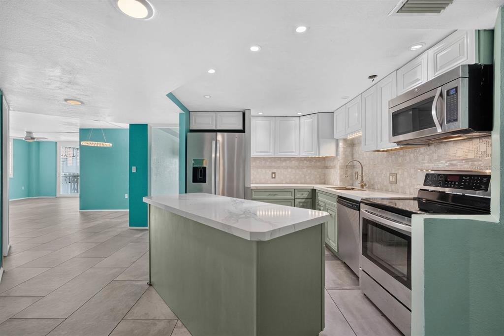 A kitchen features a green island with a marble countertop, white cabinets, and stainless appliances — 935 N HALIFAX AVENUE UNIT 406, DAYTONA BEACH, FL
