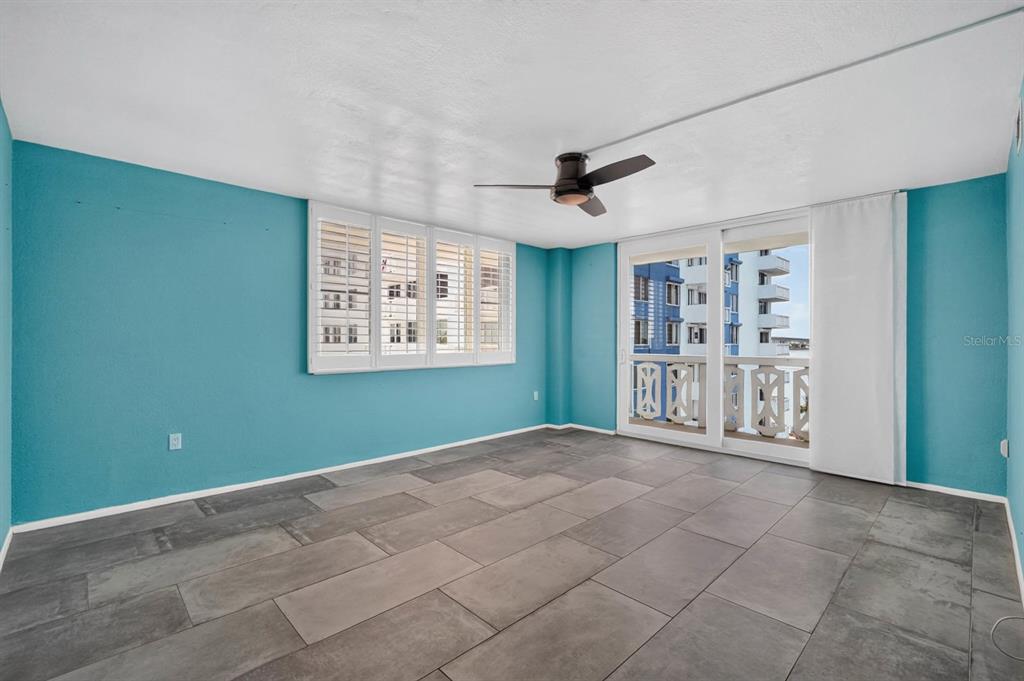 An empty room with teal walls, large gray floor tiles, and a sliding glass door — 935 N HALIFAX AVENUE UNIT 406, DAYTONA BEACH, FL