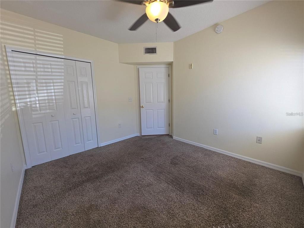 An empty bedroom features beige walls, brown carpeting, a ceiling fan, and white closet doors — 6446 CYPRESSDALE DRIVE UNIT 102, RIVERVIEW, FL