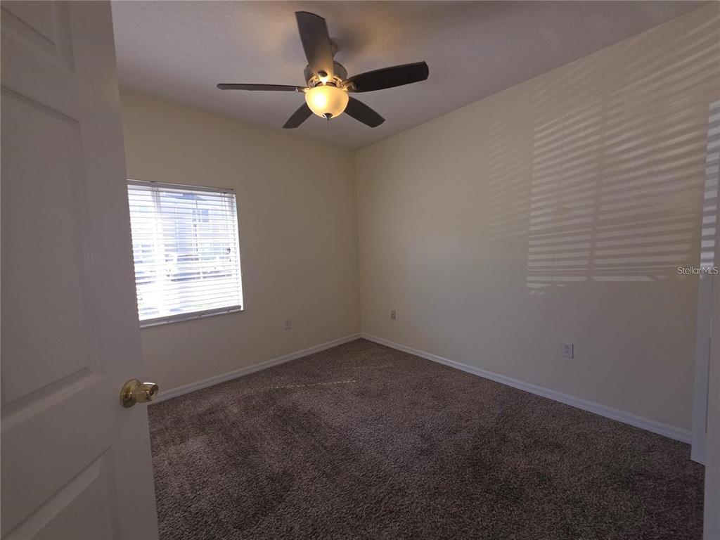 An empty bedroom features beige walls, brown carpeting, a ceiling fan, and a window with blinds — 6446 CYPRESSDALE DRIVE UNIT 102, RIVERVIEW, FL