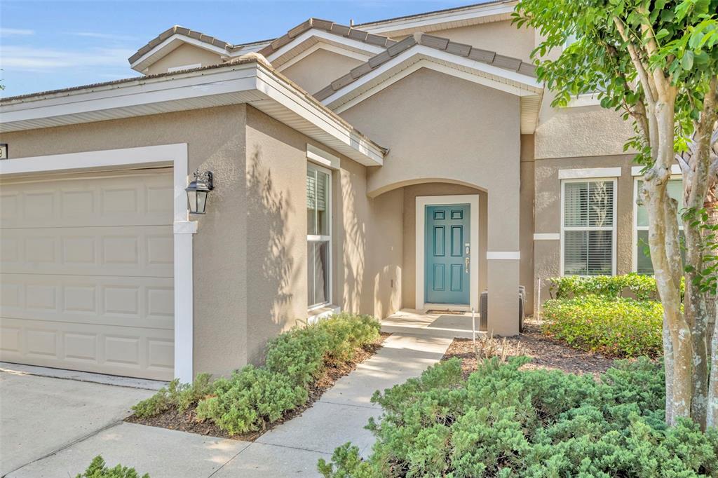 A two-story house exterior features a beige stucco facade, a blue front door, and landscaping — 4209 OAKVIEW DRIVE, DAVENPORT, FL