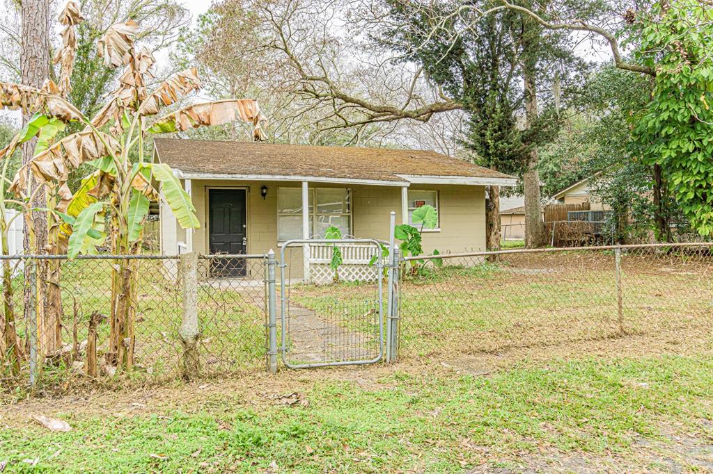 A small, tan, single-story house with a chain-link fence and banana plants in the yard — 14918 PINECREST ROAD, TAMPA, FL