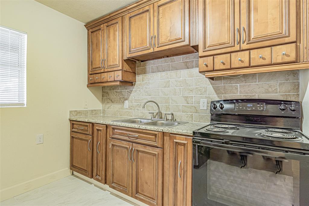 A kitchen features wood cabinets, granite countertops, a tiled backsplash, and a black electric stove — 14918 PINECREST ROAD, TAMPA, FL