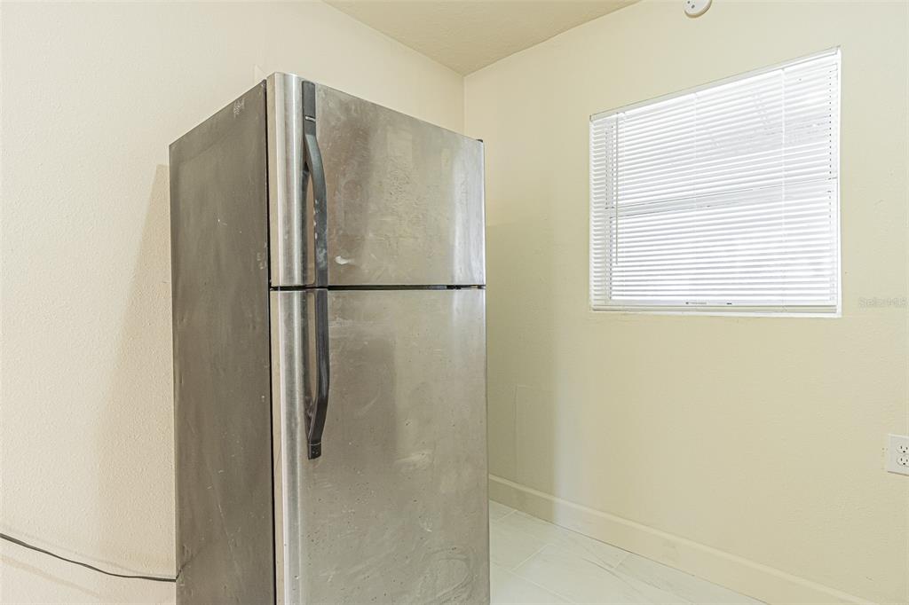 A stainless steel refrigerator stands in a corner of a room with light-colored walls — 14918 PINECREST ROAD, TAMPA, FL
