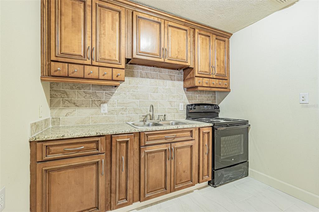 A kitchen features wood cabinets, granite countertops, a tile backsplash, and a black electric stove — 14918 PINECREST ROAD, TAMPA, FL