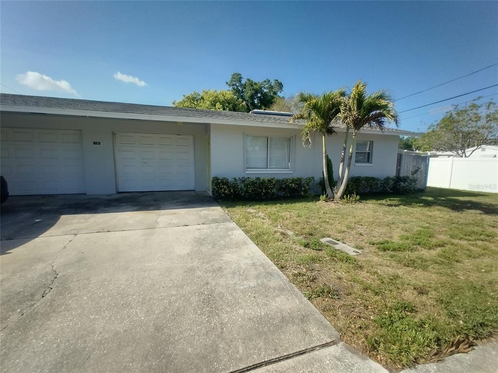 A single-story house features a concrete driveway, two garage doors, and a small palm tree — 1388 ROBIN HOOD LANE UNIT 1141-B, DUNEDIN, FL