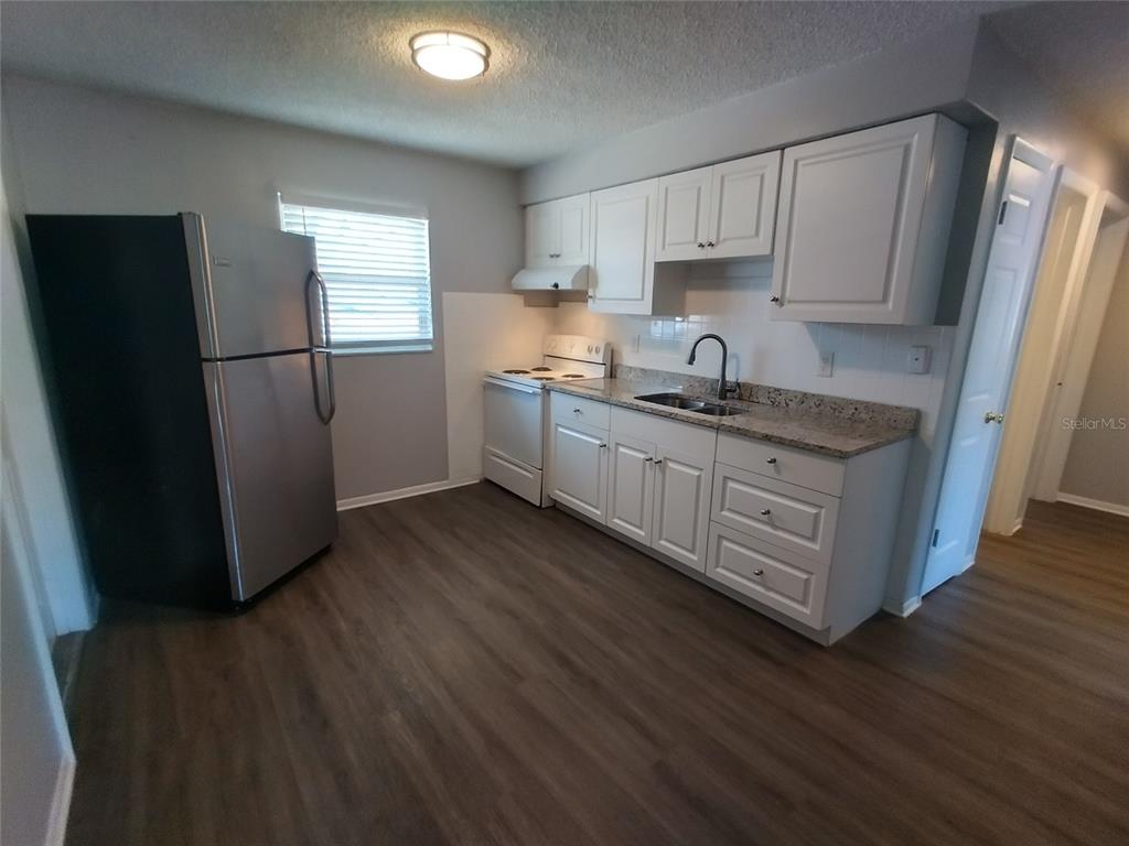 A kitchen features white cabinets, stainless steel appliances, granite countertops, and wood-look flooring — 1388 ROBIN HOOD LANE UNIT 1141-B, DUNEDIN, FL