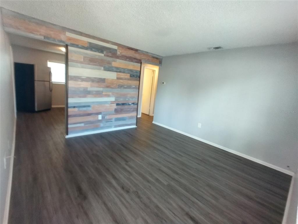 An interior view of a living room featuring wood-look flooring and a wood-paneled accent wall — 1388 ROBIN HOOD LANE UNIT 1141-B, DUNEDIN, FL