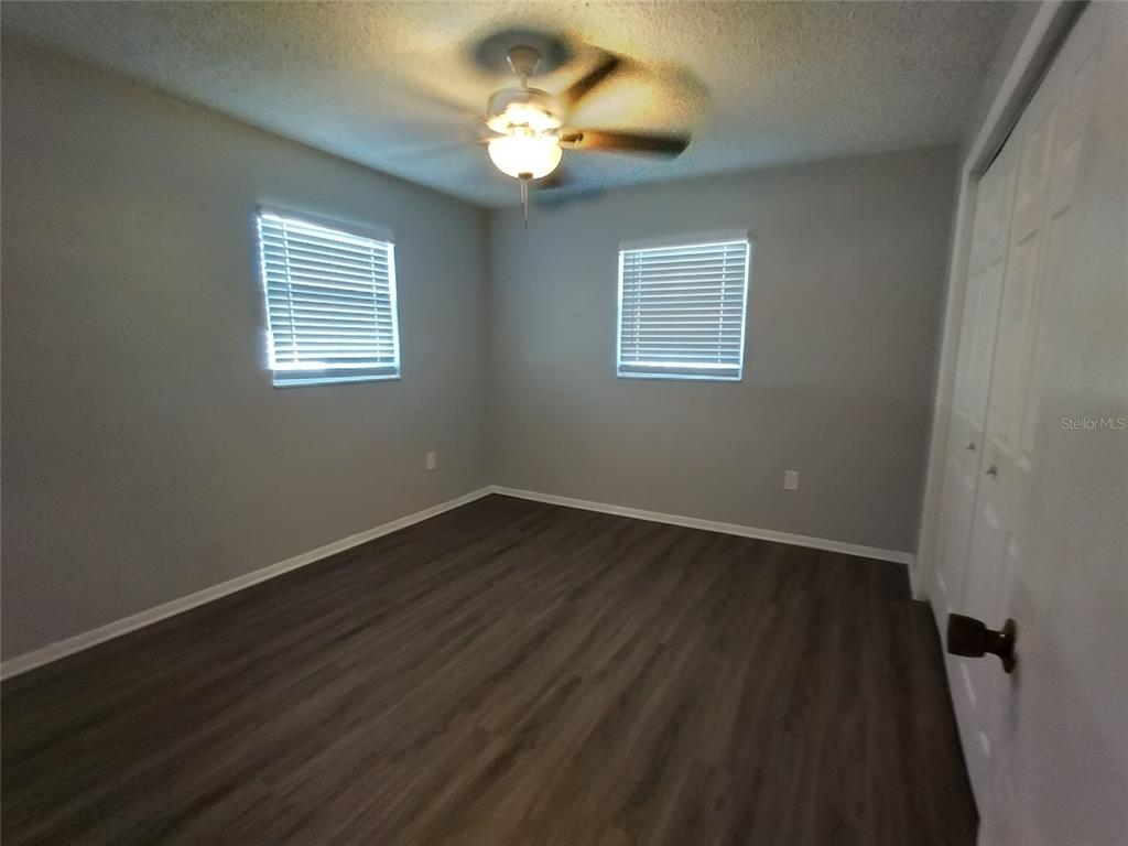 An empty bedroom features gray walls, wood-look flooring, two windows with blinds, and a ceiling fan — 1388 ROBIN HOOD LANE UNIT 1141-B, DUNEDIN, FL