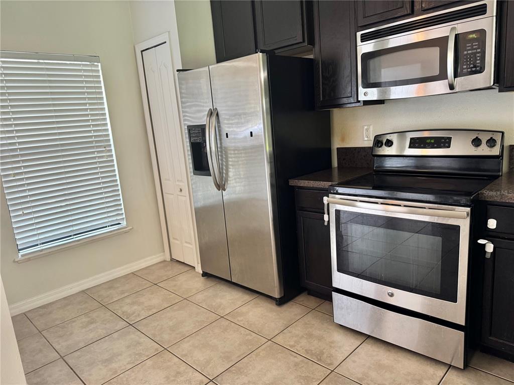 A kitchen features dark wood cabinets, stainless steel appliances, and light-colored tile flooring — 3141 WINDLESHORE WAY, SANFORD, FL