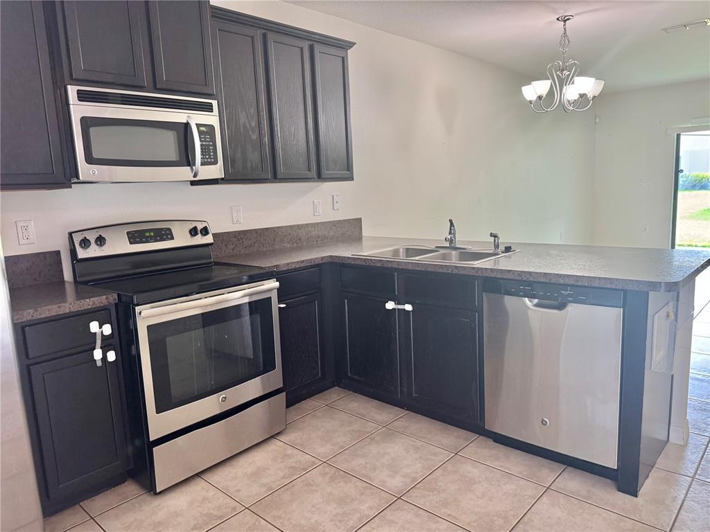 A kitchen features dark wood cabinets, stainless steel appliances, and a tiled floor — 3141 WINDLESHORE WAY, SANFORD, FL