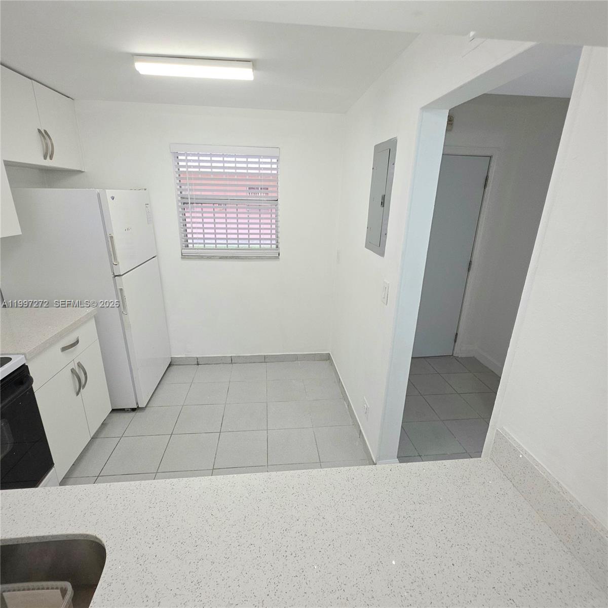 A kitchen features white cabinets, a white refrigerator, a window, and light-colored tile flooring — 19771 SW 114th Ave # 129, Miami FL 33157, MIAMI, FL