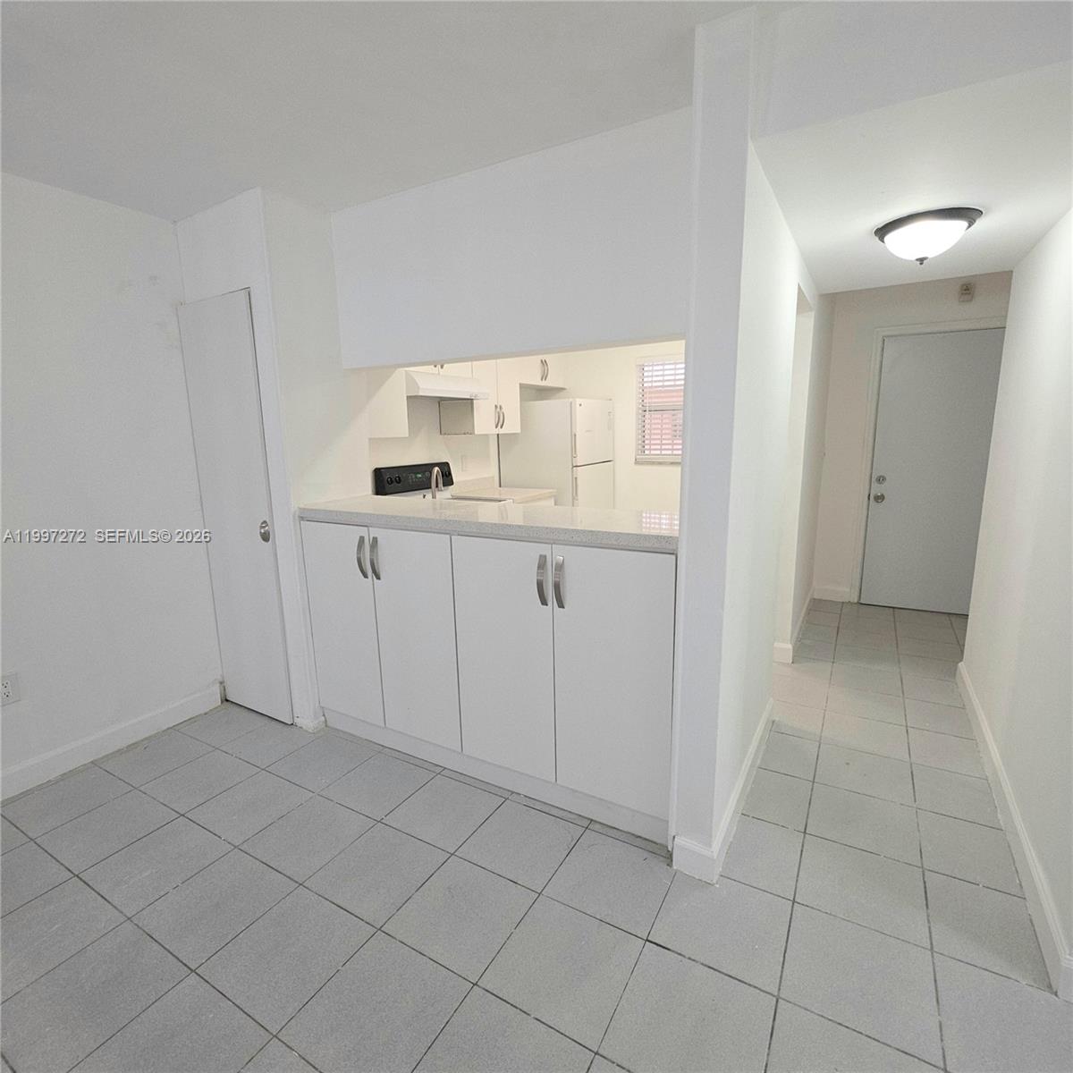 A small kitchen features white cabinets, a pass-through window, and light-colored tile flooring — 19771 SW 114th Ave # 129, Miami FL 33157, MIAMI, FL