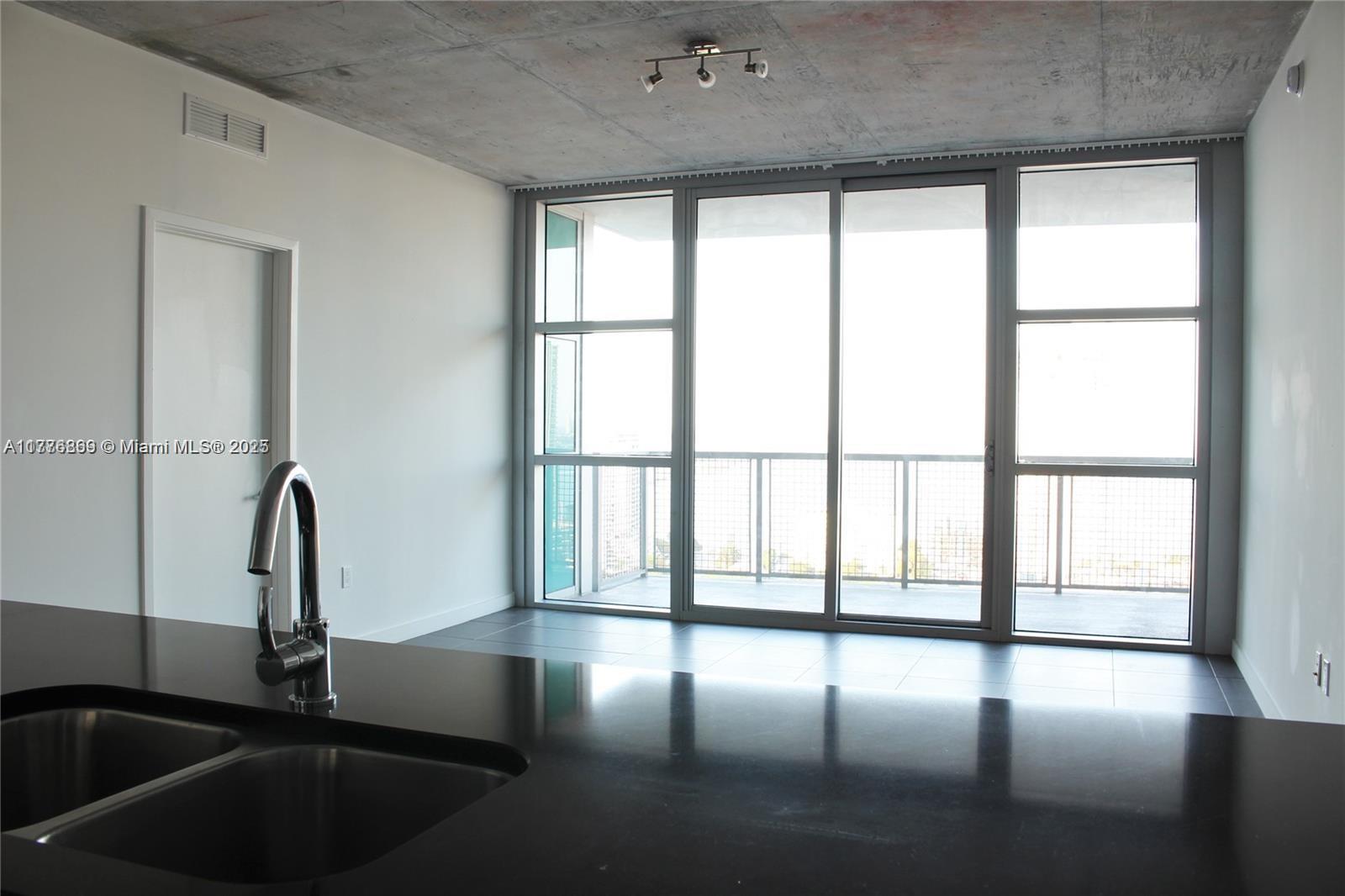 A modern kitchen with a black countertop and sink overlooks a balcony through large windows — 3301 NE 1 AV # H2904, Miami FL 33137, MIAMI, FL