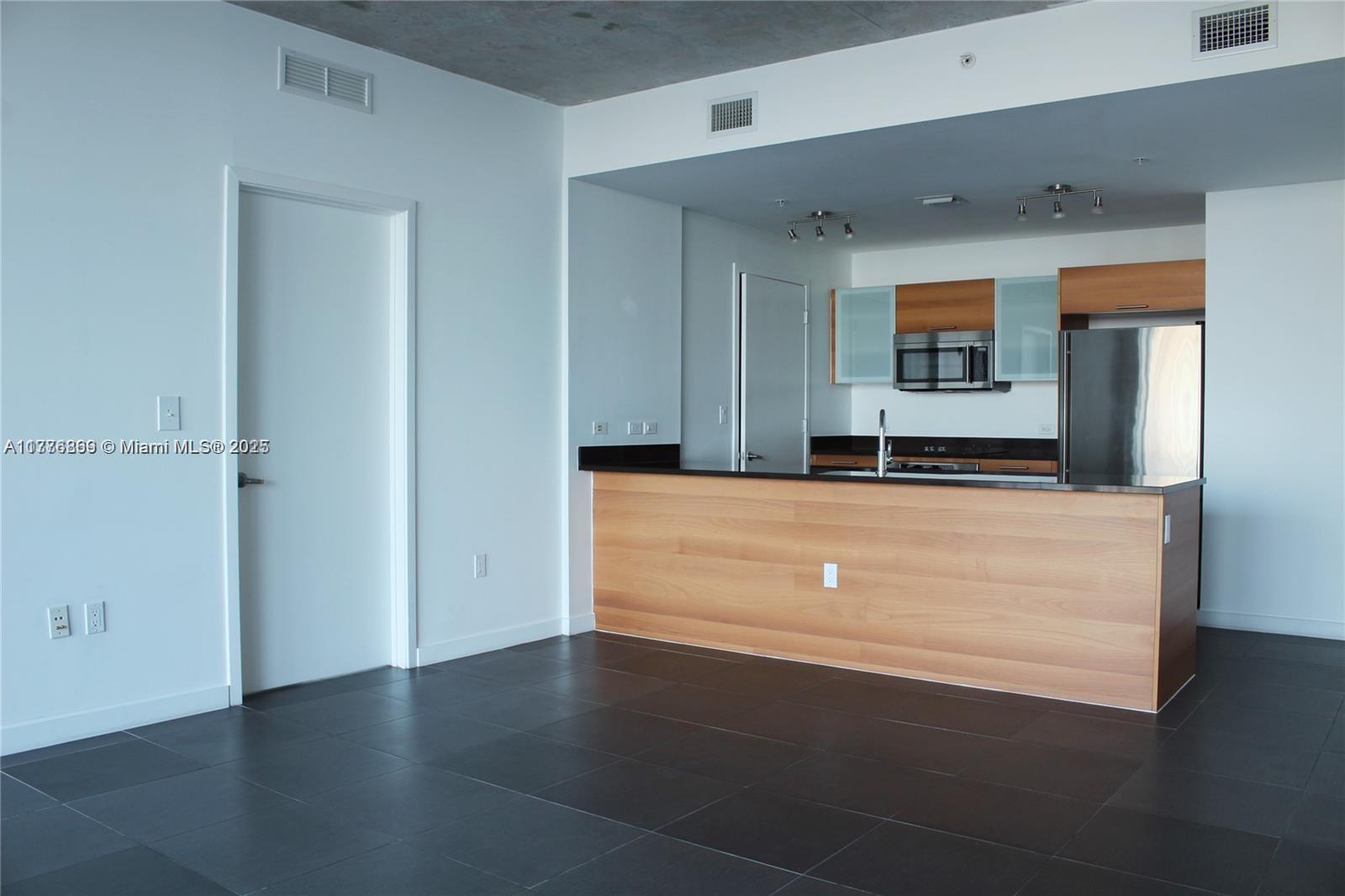 A kitchen with wood cabinets and a breakfast bar overlooks a room with tile floors — 3301 NE 1 AV # H2904, Miami FL 33137, MIAMI, FL