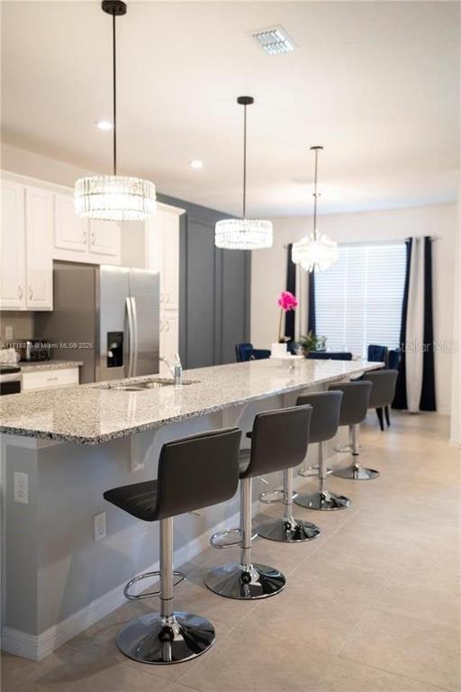 A kitchen island with bar stools sits in front of white cabinets and pendant lights — 2183 COPPER BELL PLACE, KISSIMMEE, FL