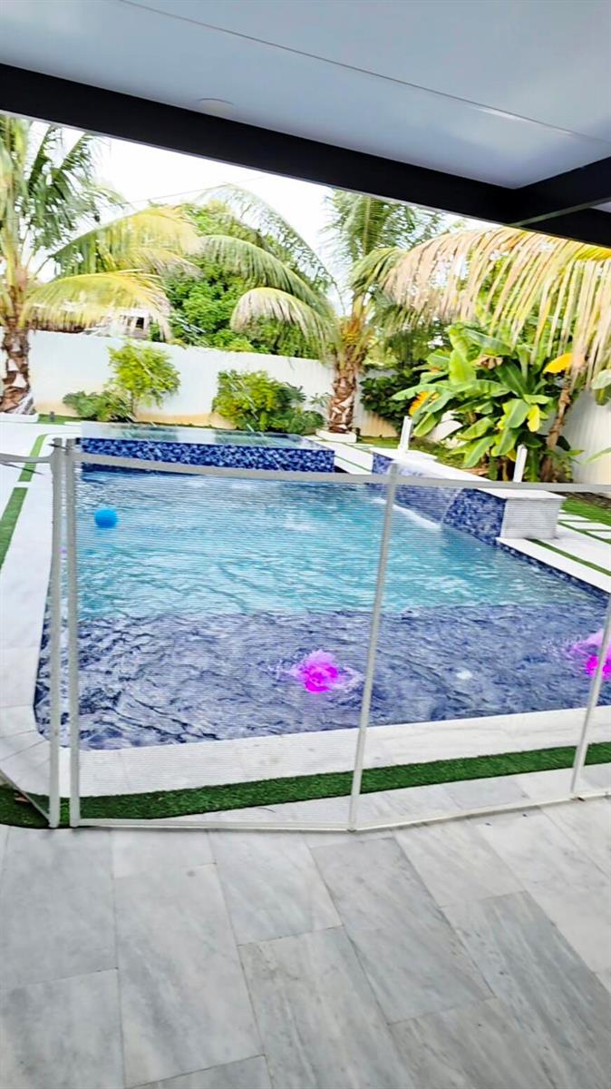 A backyard swimming pool with a spa, fountains, and lounge chairs on a stone patio — 1902 Baythorne Road, West Palm Beach FL 33415, WEST PALM BEACH, FL