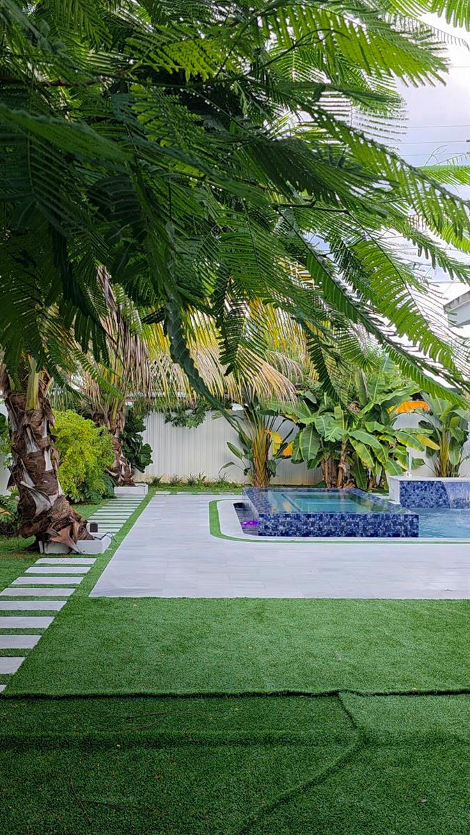 A rectangular swimming pool with a raised tiled spa and a waterfall feature in a backyard — 1902 Baythorne Road, West Palm Beach FL 33415, WEST PALM BEACH, FL