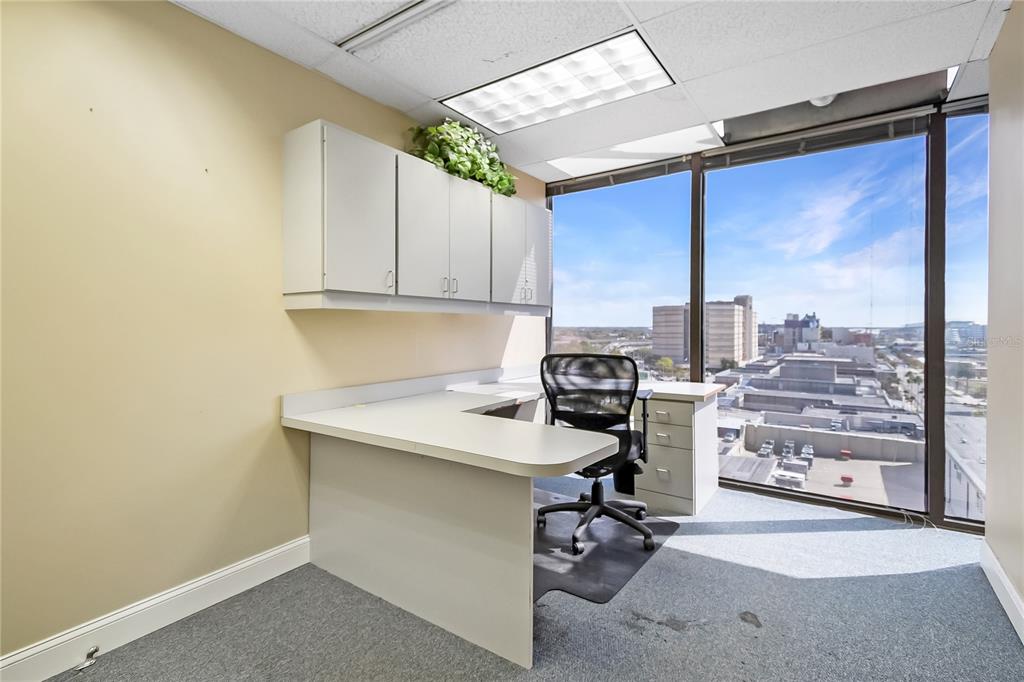 An office with a white L-shaped desk, wall-mounted cabinets, and floor-to-ceiling windows overlooking a city — 233 E BAY STREET UNIT 1016, JACKSONVILLE, FL