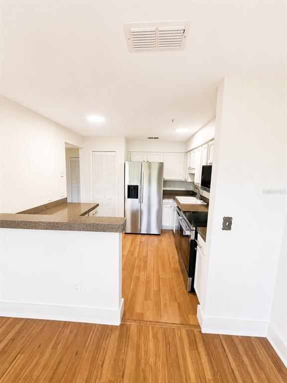 A kitchen features stainless steel appliances, white cabinets, dark countertops, and light wood-look flooring — 920 LOCH CARRON UNIT 16, APOPKA, FL