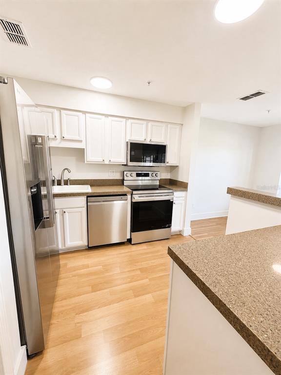 A kitchen features white cabinets, stainless steel appliances, and brown countertops over wood-look flooring — 920 LOCH CARRON UNIT 16, APOPKA, FL