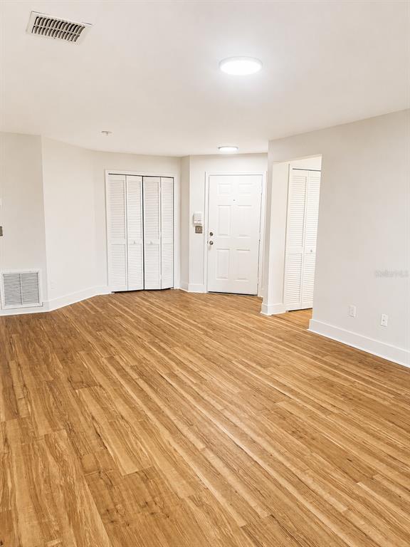 An empty room features light wood-look flooring, white walls, two sets of louvered closet doors, and a front door — 920 LOCH CARRON UNIT 16, APOPKA, FL