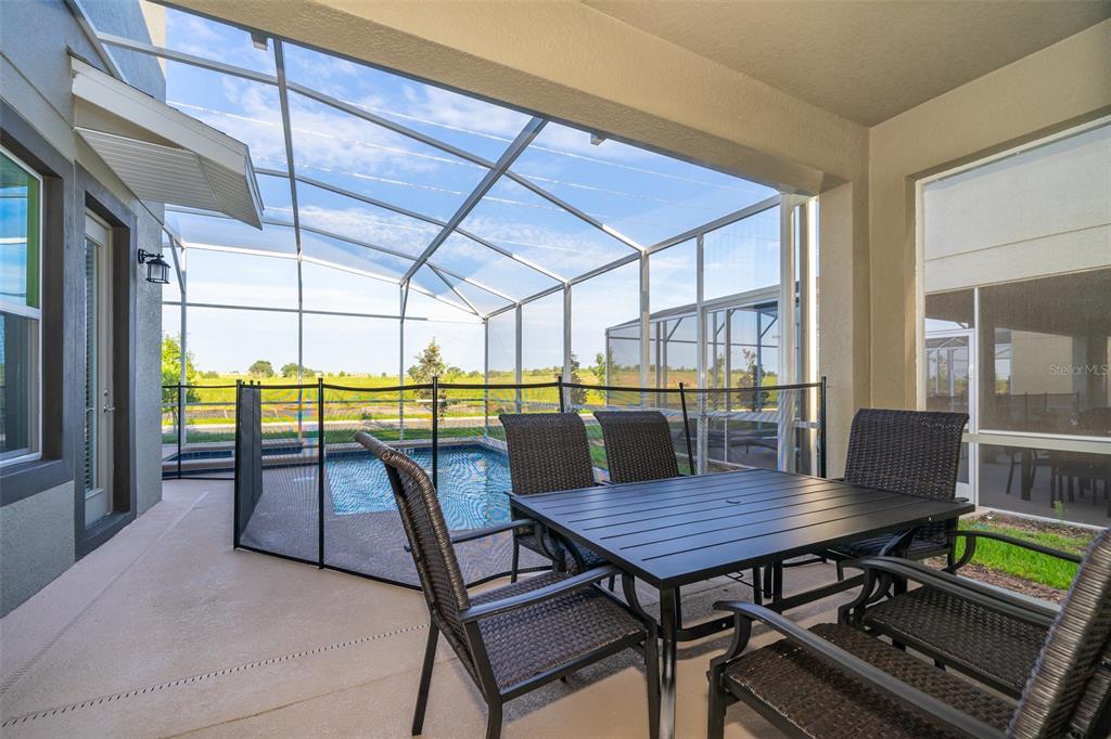 A covered patio with a dining set overlooks a screened-in pool and a grassy field — 800 STICKS STREET, DAVENPORT, FL